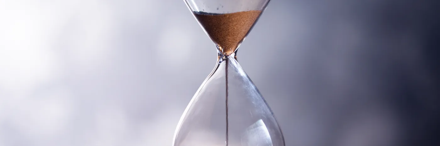 An hourglass running down on a table, lit from behind.