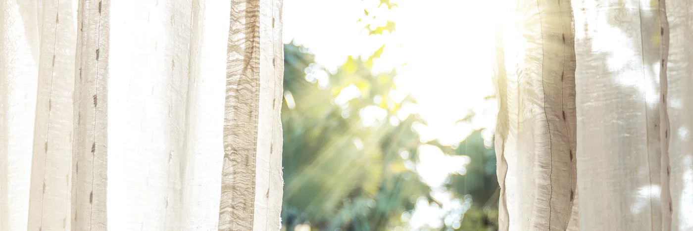 Morning sunlight coming through white linen curtains at an open door.